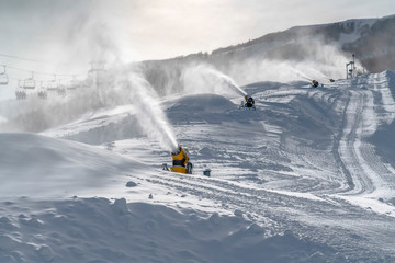 Snow guns and ski lifts on snowy slope
