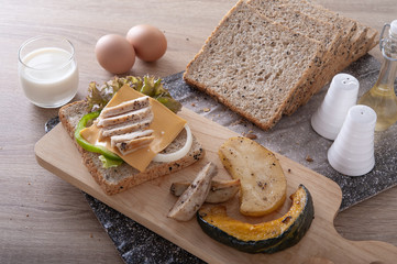 Sandwich grilled breast chicken with cheese, vegetable and whole grain bread on wooden board for breakfast