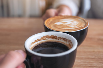 Close up image of a man and a woman clinking two coffee mugs on wooden table in cafe