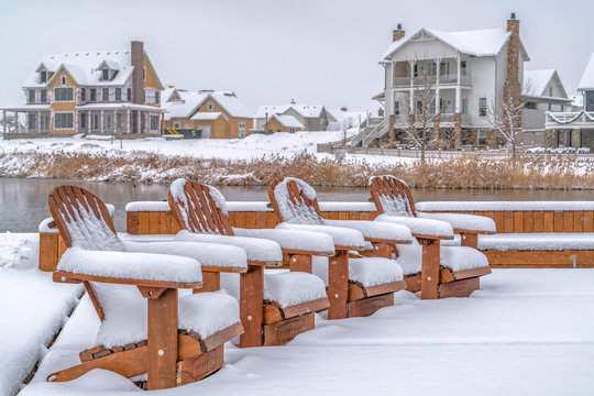 Snowy chairs on a lake deck against homes in Utah