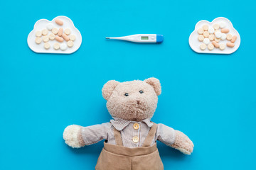 Childhood diseases concept. Treatment of children.Teddy bear toy, thermometer and pills on blue background top view space for text