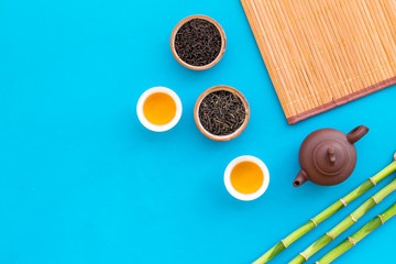 Chinese tea ceremony concept. Tea pot, tea cup, dry tea leaves, bamboo mat on blue background top view copy space pattern
