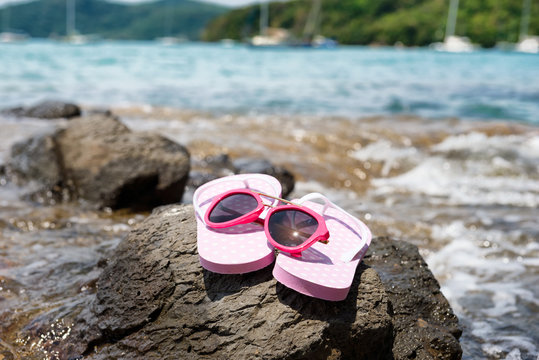 Pink thongs shoes of women and sunglasses stand it down on the rocks beach. Travel & tours for relaxing in summer concept.
