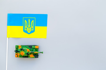 War, military threat, military power concept. Ukraine. Tanks toy near Ukrainian flag on grey...