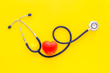Heart health, health care concept. Stethoscope near rubber heart on yellow background top view copy space