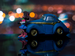 Toy girl standing at the blue car at night.