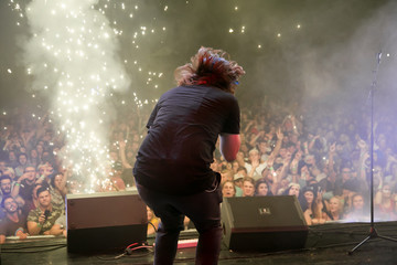 musician on stage in front of crowd of people with pyro sparks on the side