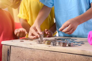 Hands of children are helping putting coins into piggy bank on white background