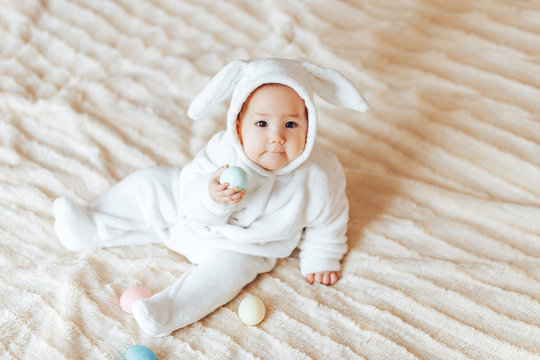 small child smiling baby in a white bunny rabbit costume easter playing with colorful easter eggs