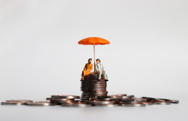 An elderly miniature couple sitting with an umbrella on a pile of coins.