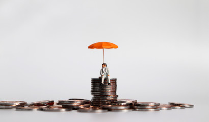 An elderly miniature man sitting with an umbrella on a pile of coins.