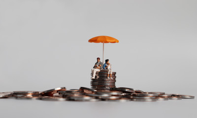 A miniature couple holding a baby sitting with an orange umbrella on a pile of coins. © Hyejin Kang