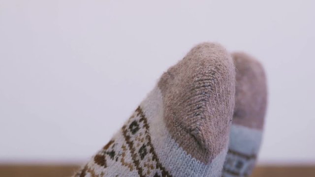 A woman in warm knitted socks does morning exercises, while sitting stretches her fingers up to her toes.