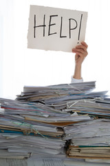 Person under a pile of papers with a hand holding a sign of help. Accounting.