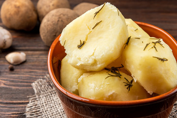 Boiled potato in brown bowl on dark wooden background.