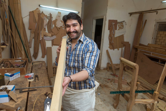 Smiling carpenter in his workshop checking the straightness of a wooden log.	