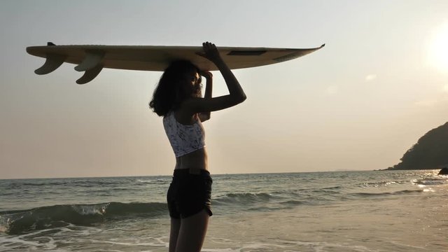 Silhouette of surfer girl standing with surf board on the tropical beach at sunset