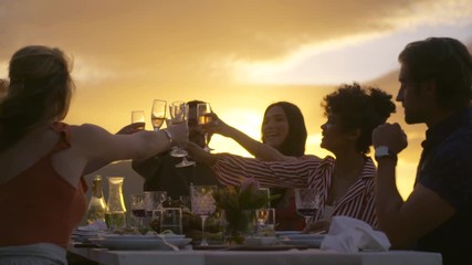 Diverse group of friends sitting at dinner table and toasting drinks at party. Young people enjoying drinks at dinner out in the yard. - Powered by Adobe