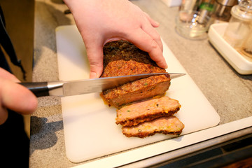 Woman hands cutting piece of meatloaf, she prepare for tasting of food at kitchen. Chef cutting meatloaf with knife on board on restaurant kitchen table. Housewife sliced meatloaf on cutting board.