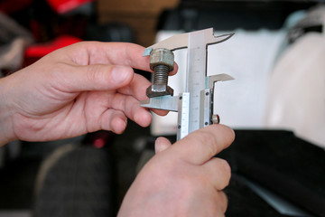 Worker with tools in hands. Mechanic is checking and measuring screw size with stainless steel caliper in automechanics workshop, car garage. Hands of mechanic holding steel screw using steel caliper.