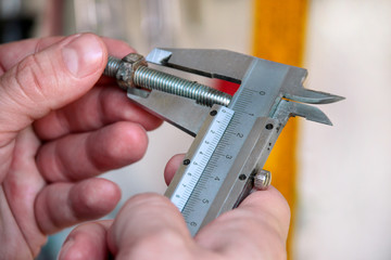 Worker with tools in hands. Mechanic is checking and measuring screw size with stainless steel caliper in automechanics workshop, car garage. Hands of mechanic holding steel screw using steel caliper.