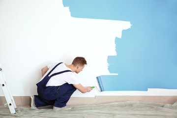Male painter using roller for refurbishing color of wall indoors - obrazy, fototapety, plakaty