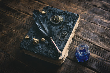 Ancient magic book, ink well and a quill pen on a wooden table background. Spell book.