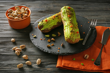 Slate plate with tasty pistachio eclairs with nuts on wooden table