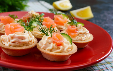 Tartlets with cream cheese and salted salmon on a red plate. Tasty light snack for a party. Finger Food. Close up