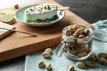 Jar with tasty pistachio nuts and ice-cream on table