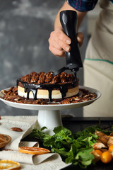 Female confectioner decorating tasty pecan cake at table