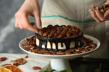 Female confectioner decorating tasty pecan cake at table, closeup
