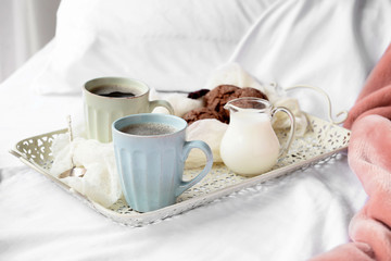 Cups of hot coffee with milk in jug and cookies on bed