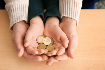 Hands of young man and his son holding coins on wooden table. Concept of child support