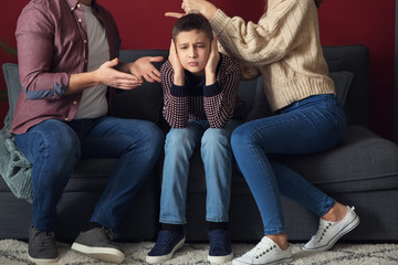 Sad little boy covering ears while his parents arguing at home