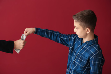 Little boy trying to take money from adult person on color background. Concept of child support