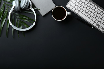 Stylish workplace with keyboard, headphones and cup of coffee on dark background - obrazy, fototapety, plakaty