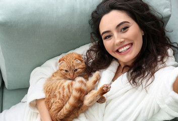 Young woman taking selfie with cute funny cat at home