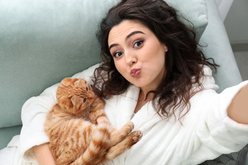 Young woman taking selfie with cute funny cat at home