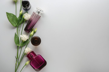 Bottles of perfume and flowers on light background