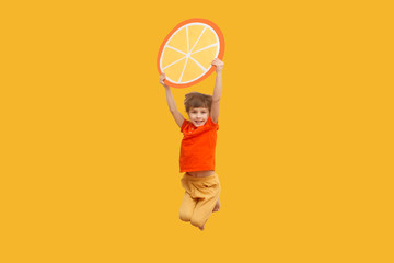Funny kid with an orange segment from a cardboard jump on a yellow background. healthy food....