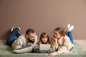 Happy family with tablet computer lying on carpet near color wall