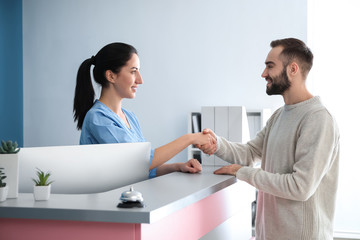 Obraz premium Young man and female receptionist shaking hands in clinic
