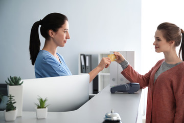 Female receptionist receiving payment for medical service from patient in clinic
