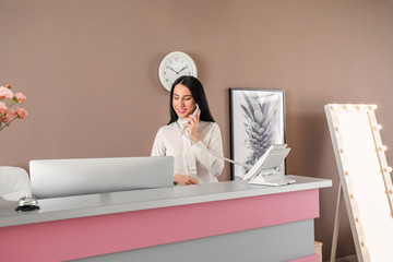 Young female receptionist talking by telephone at desk in hotel