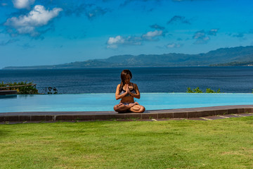 Filipina girl doing yoga poses poolside with ocean background