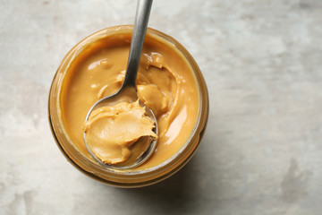 Jar and spoon with tasty peanut butter on grey background