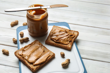 Toasted bread with tasty peanut butter on white wooden table