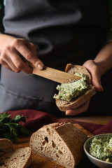 Young woman spreading green butter on piece of fresh bread at table
