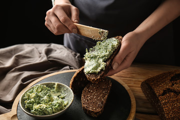 Young woman spreading green butter on piece of fresh bread at table